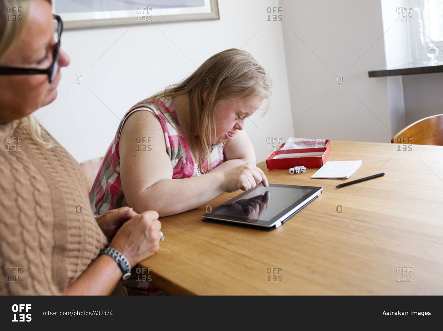 Daughter with Down syndrome using digital tablet, mother looking