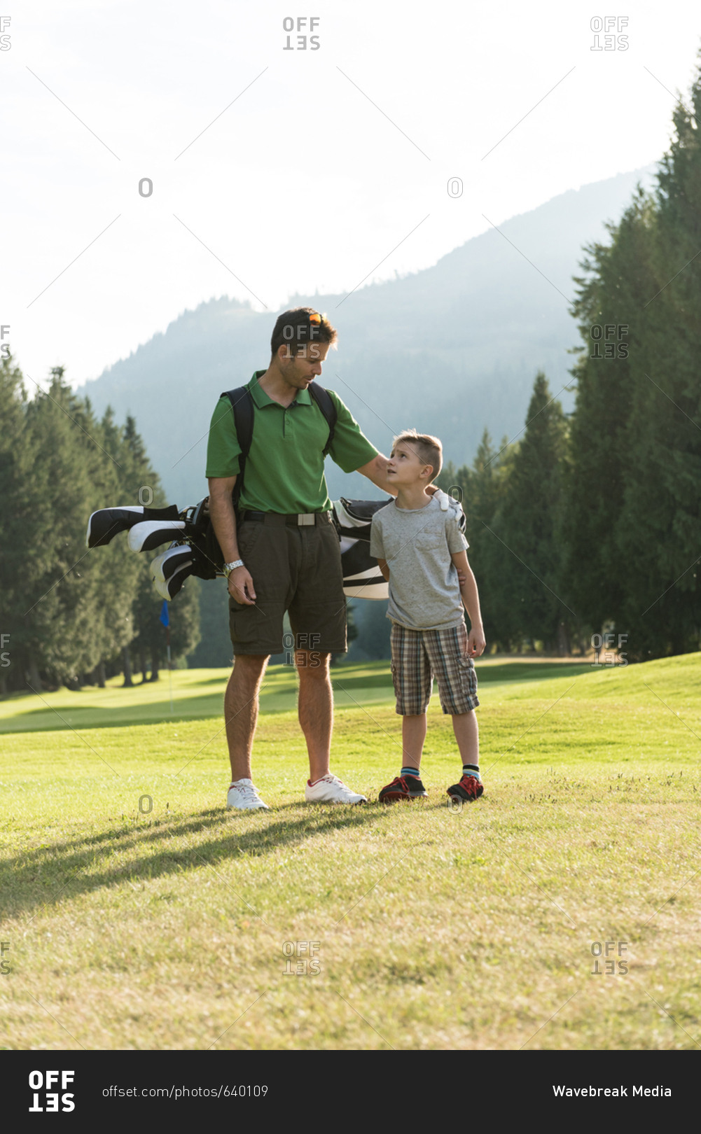 Father and son with golf bag interacting with each other in the course