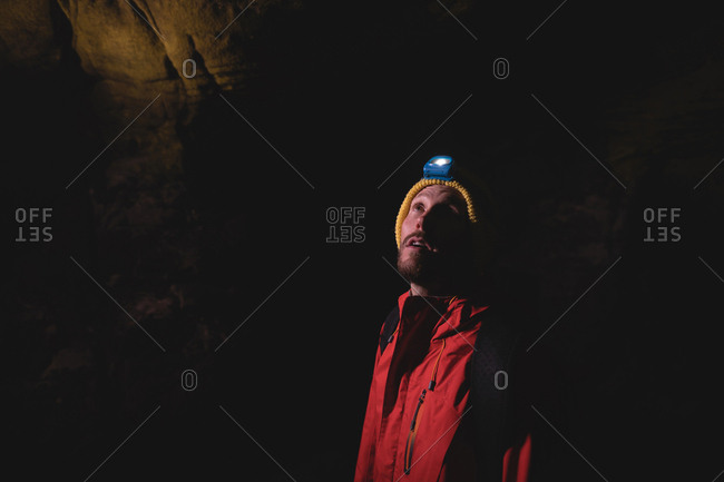 Hiker standing inside the dark cave wearing head torch with backpack