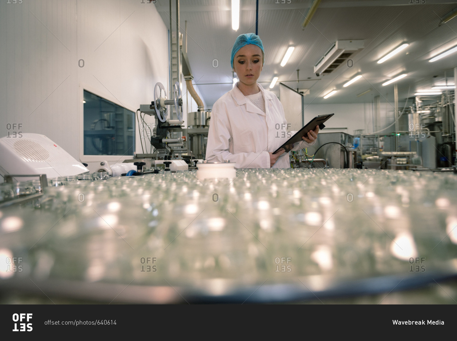 Female worker monitoring the glass jars on the production line