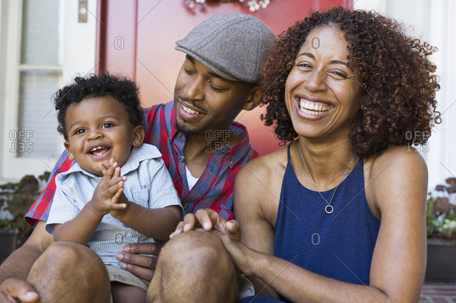 Laughing mixed race couple sitting on front stoop with son