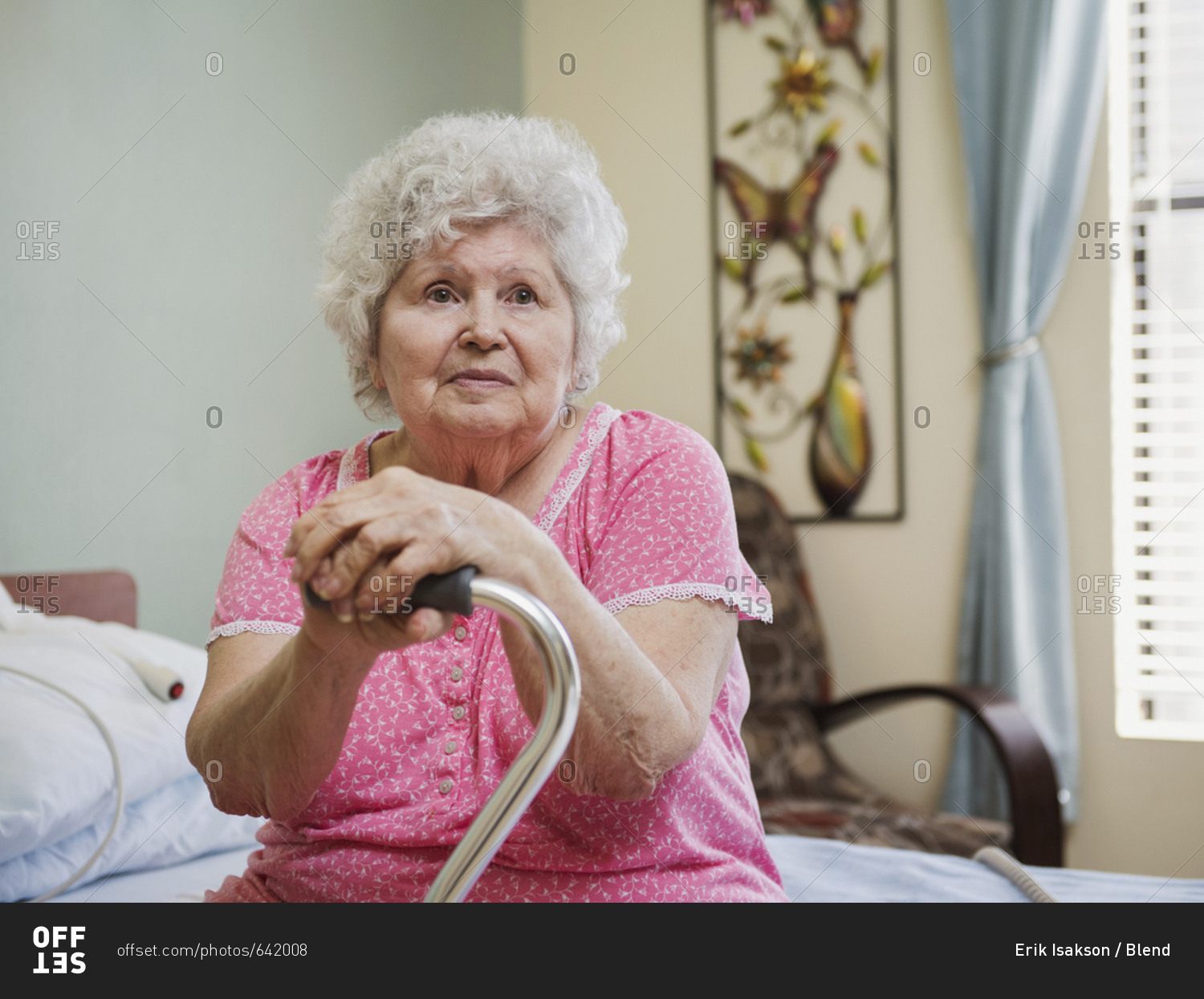 Serious Caucasian woman sitting on bed leaning on cane