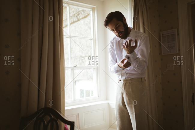 Groom getting dressed at home near the window