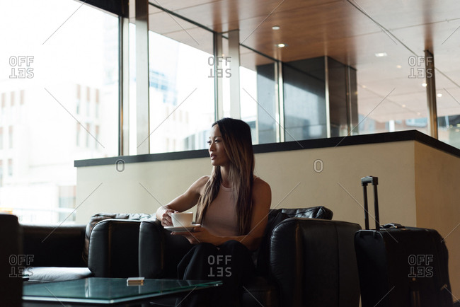 Businesswoman sitting alone looking away while having coffee in the lobby