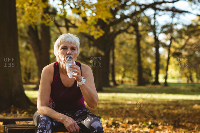 Senior woman drinking water in the park on a sunny day