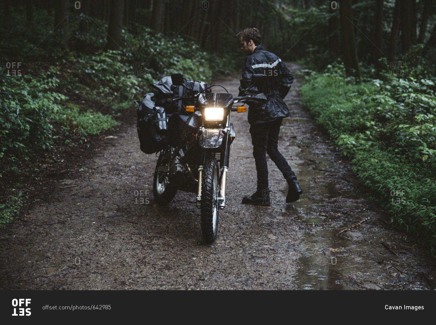 Biker wearing raincoat while standing by motorcycle in forest