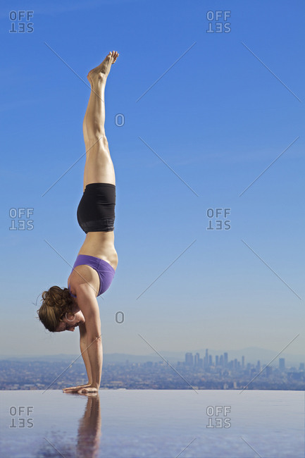 Side view of woman doing handstand on infinity pool against blue sky