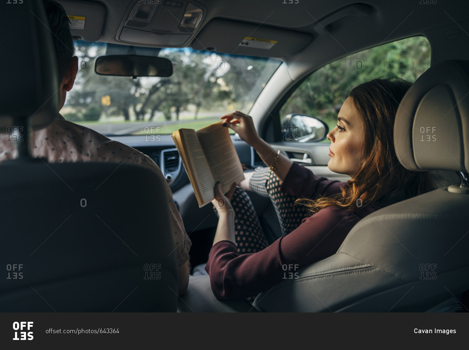 Wife reading book while traveling with husband in car