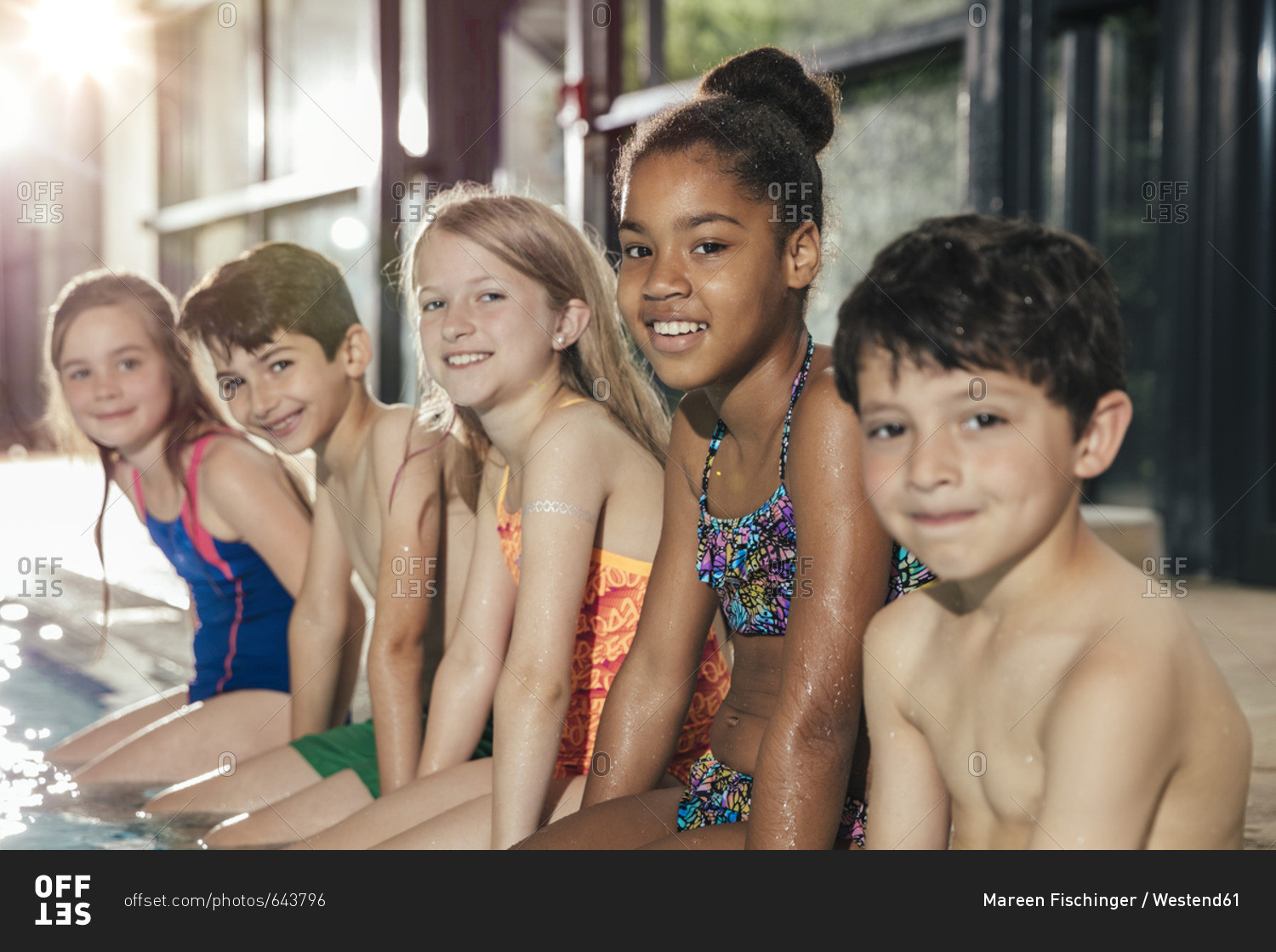 Portrait of smiling children sitting on poolside in indoor swimming pool