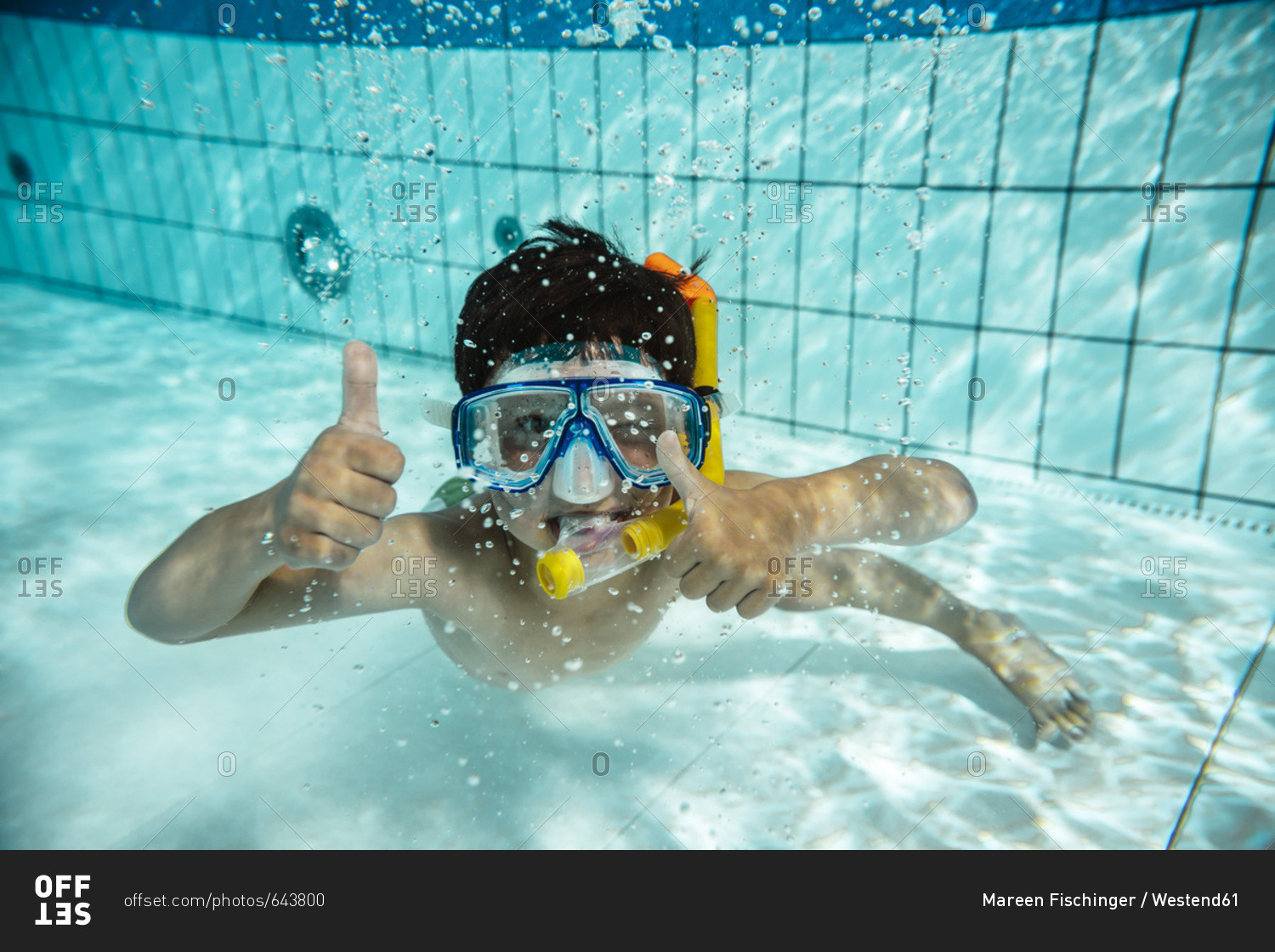 Boy with diving goggles and snorkel under water in swimming pool