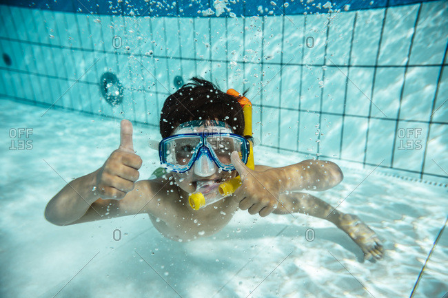 Boy with diving goggles and snorkel under water in swimming pool