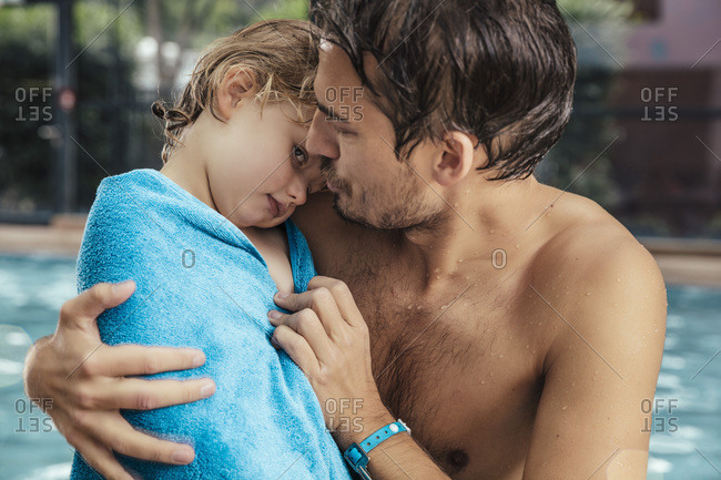 Father toweling daughter at the poolside of an indoor swimming pool