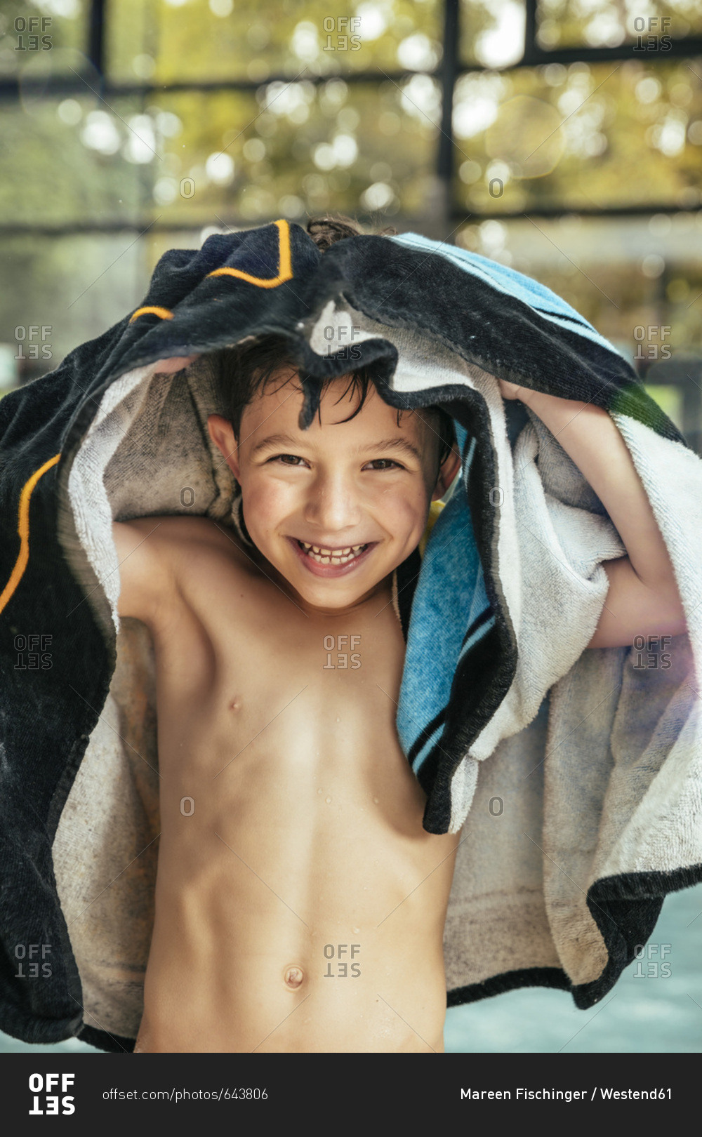 Portrait of happy boy toweling himself at the poolside of an indoor swimming pool