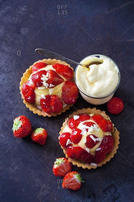 Two strawberry tartlets with custard and white chocolate shaving on dark ground