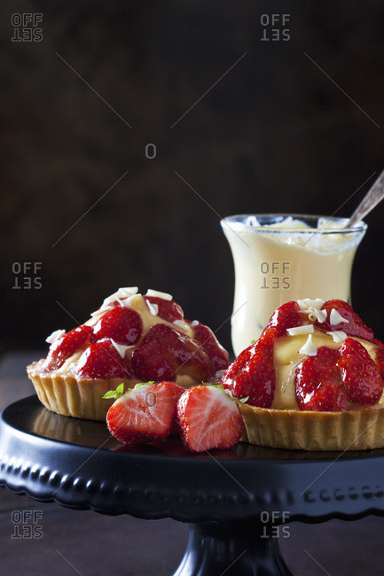 Two strawberry tartlets with custard and white chocolate shaving on cake stand
