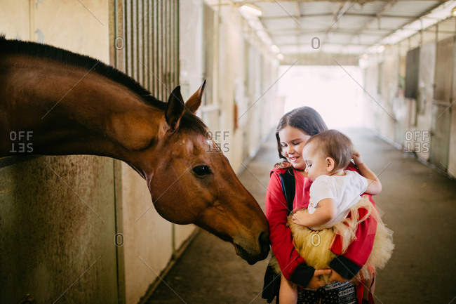 Girl holding little sister in a horse stable