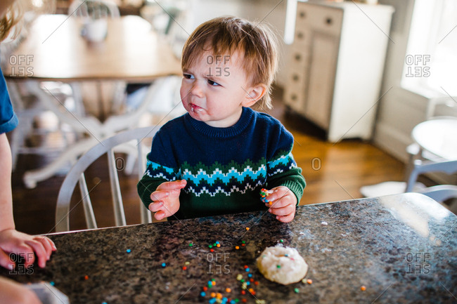 Frowning toddler boy decorating cookies