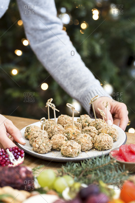 A woman is photographed as she is placing a plate of baked goat cheese balls on a plate