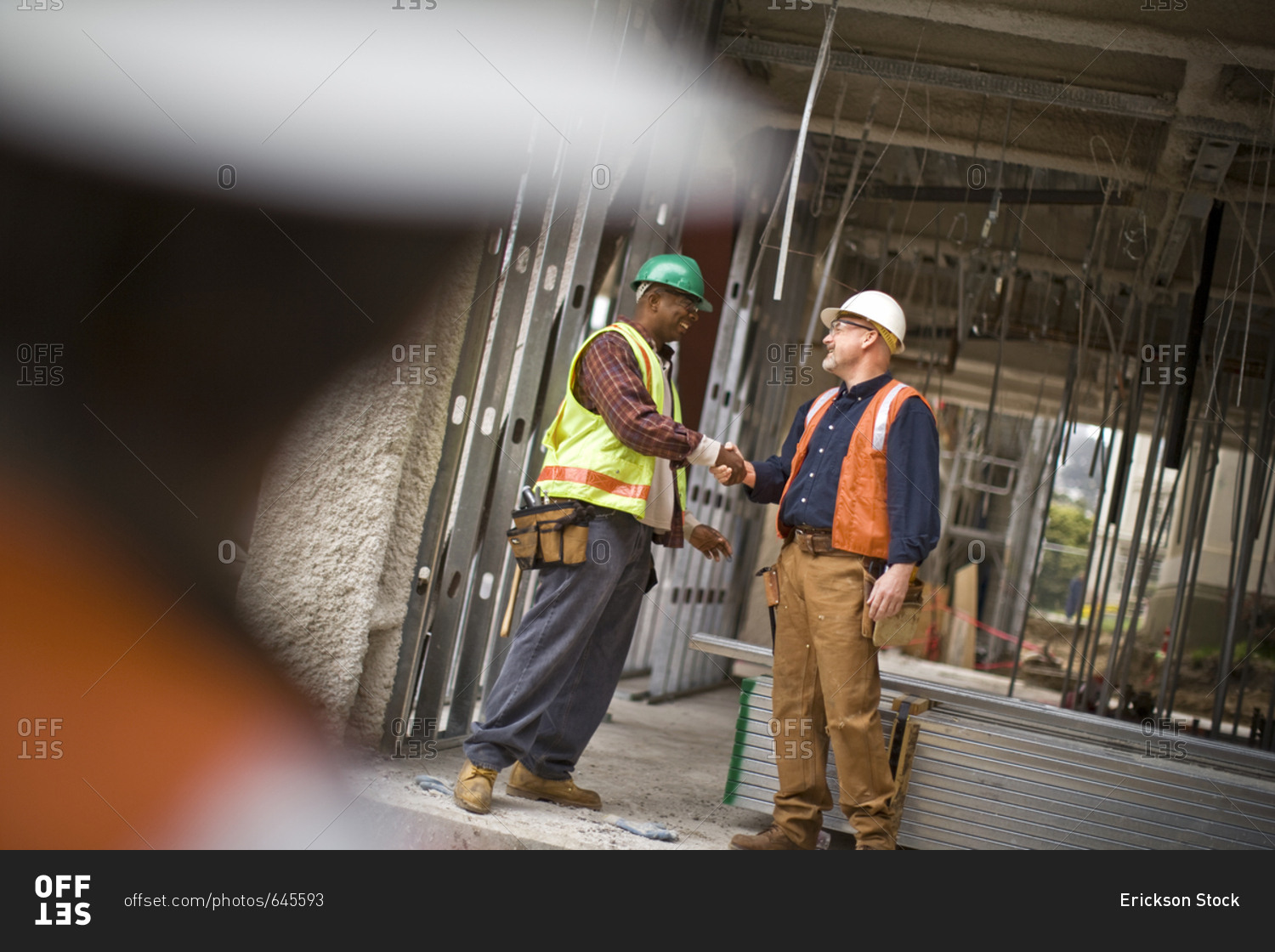 Mature male construction worker shaking hands with a mid-adult co-worker on a building site