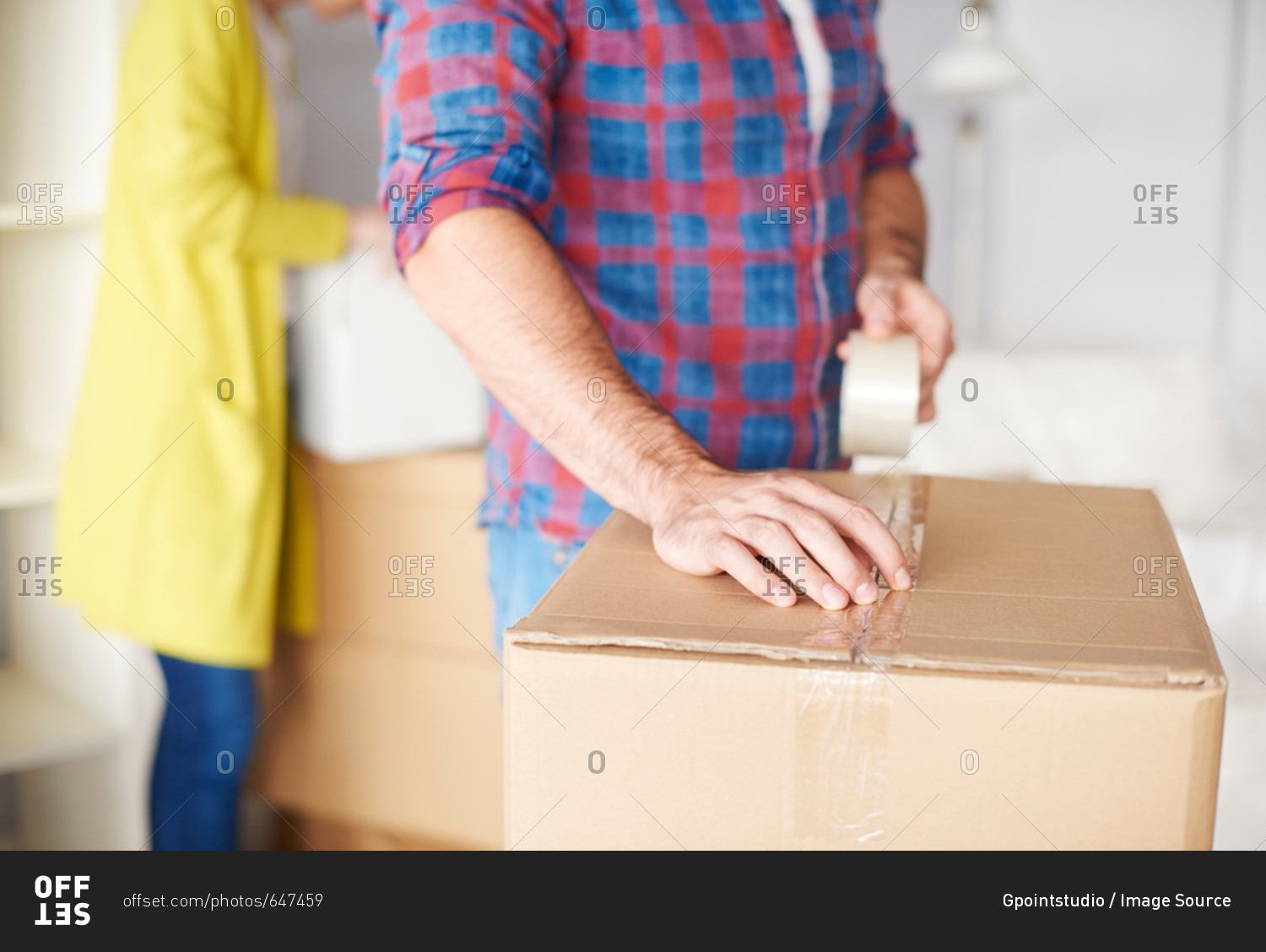 Young couple moving home, young man taping up cardboard box, mid section