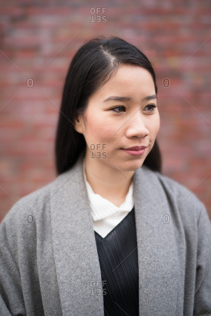 Extremely shallow depth of field portrait of young woman with black hair looking off camera in front of a brick wall
