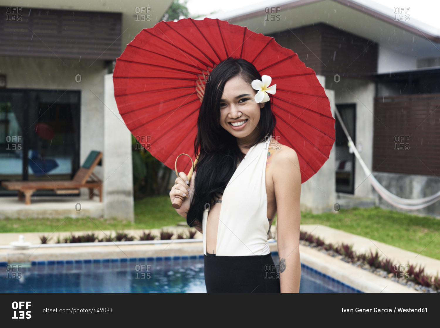 Portrait of smiling woman with flower in her hair holding a red traditional umbrella at a swimming pool