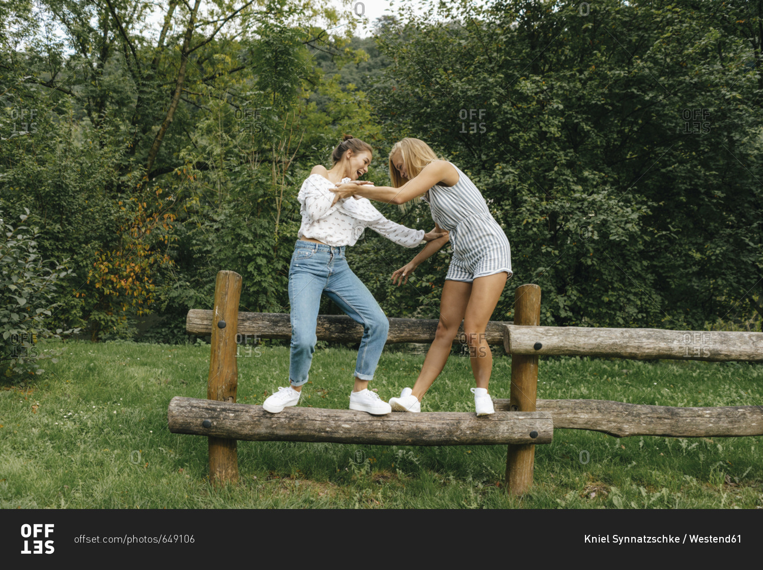 Two happy young women balancing on fence in a park