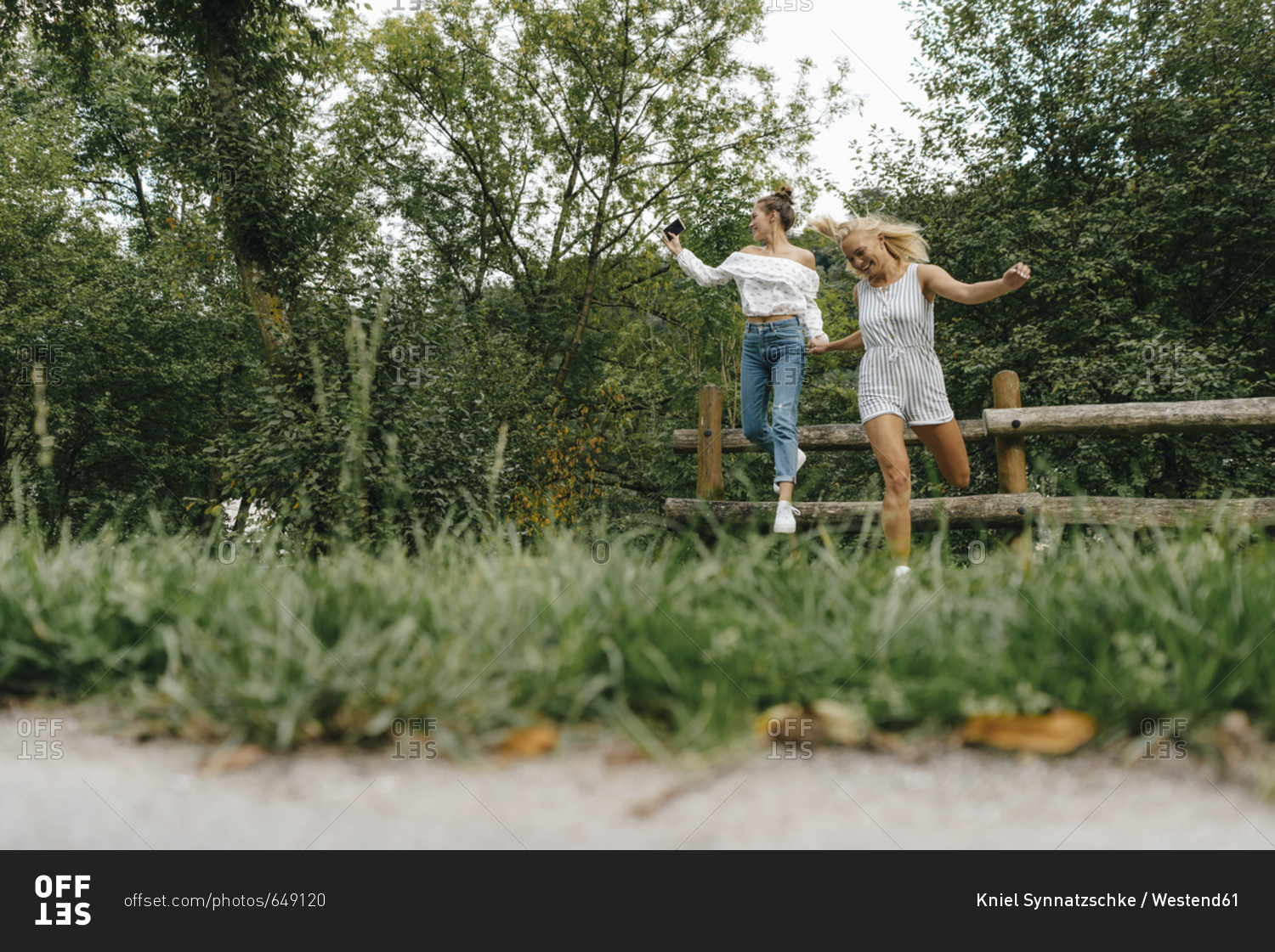 Two happy young women jumping from fence in a park