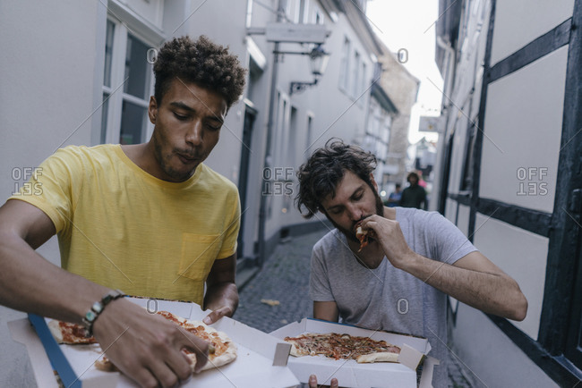 Two friends eating takeaway pizza in the city