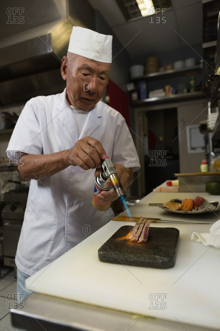 Chef heating seafood with burner in kitchen