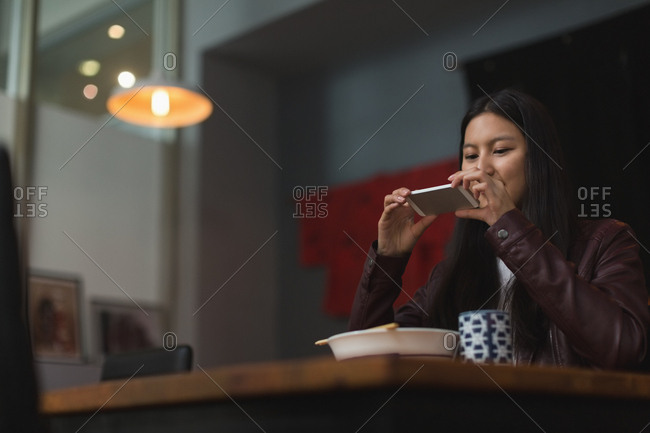 Woman taking photo of meal with mobile phone in restaurant