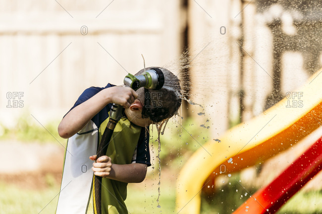 Young boy showering with hose in backyard