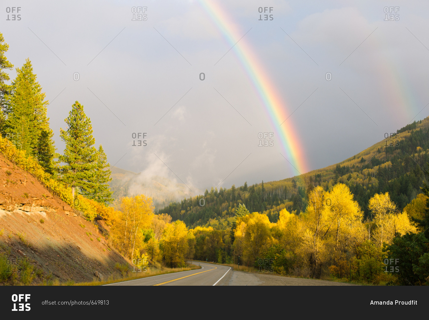 Rainbow over winding road and hills covered in Aspen trees