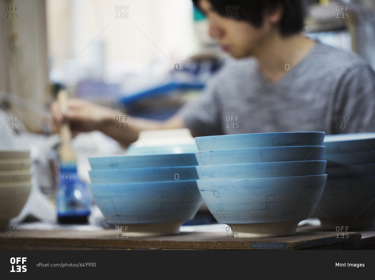Close up of man working in a Japanese porcelain workshop, painting white bowls with blue glaze