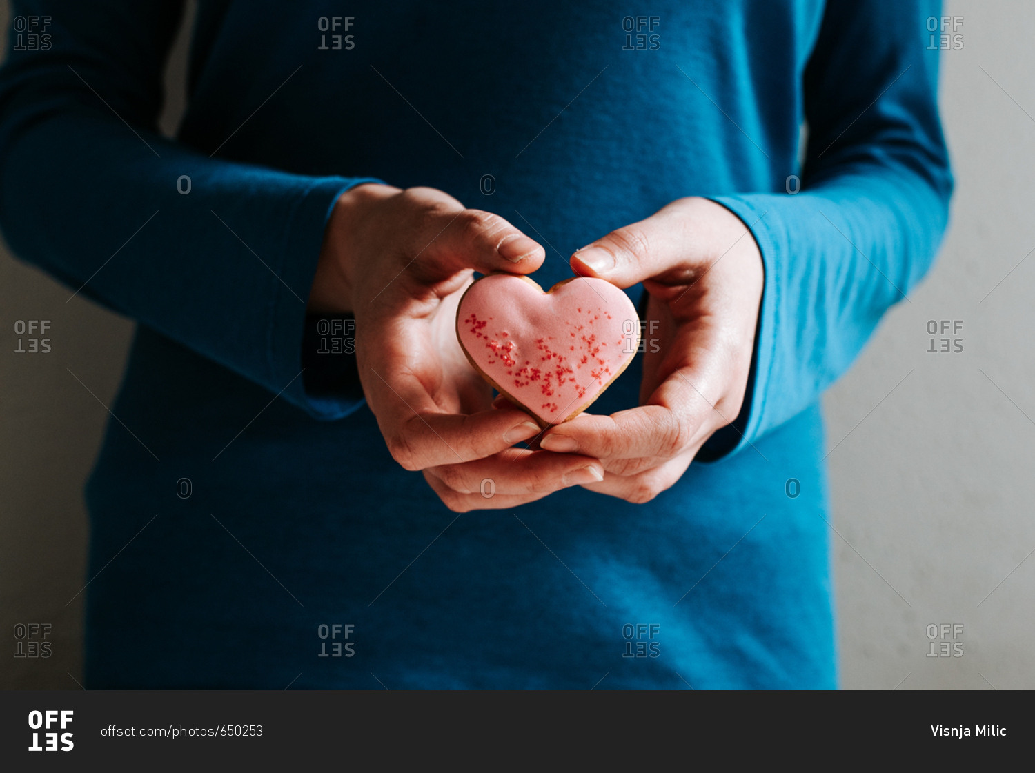 Hands holding pink heart-shaped gingerbread cookie