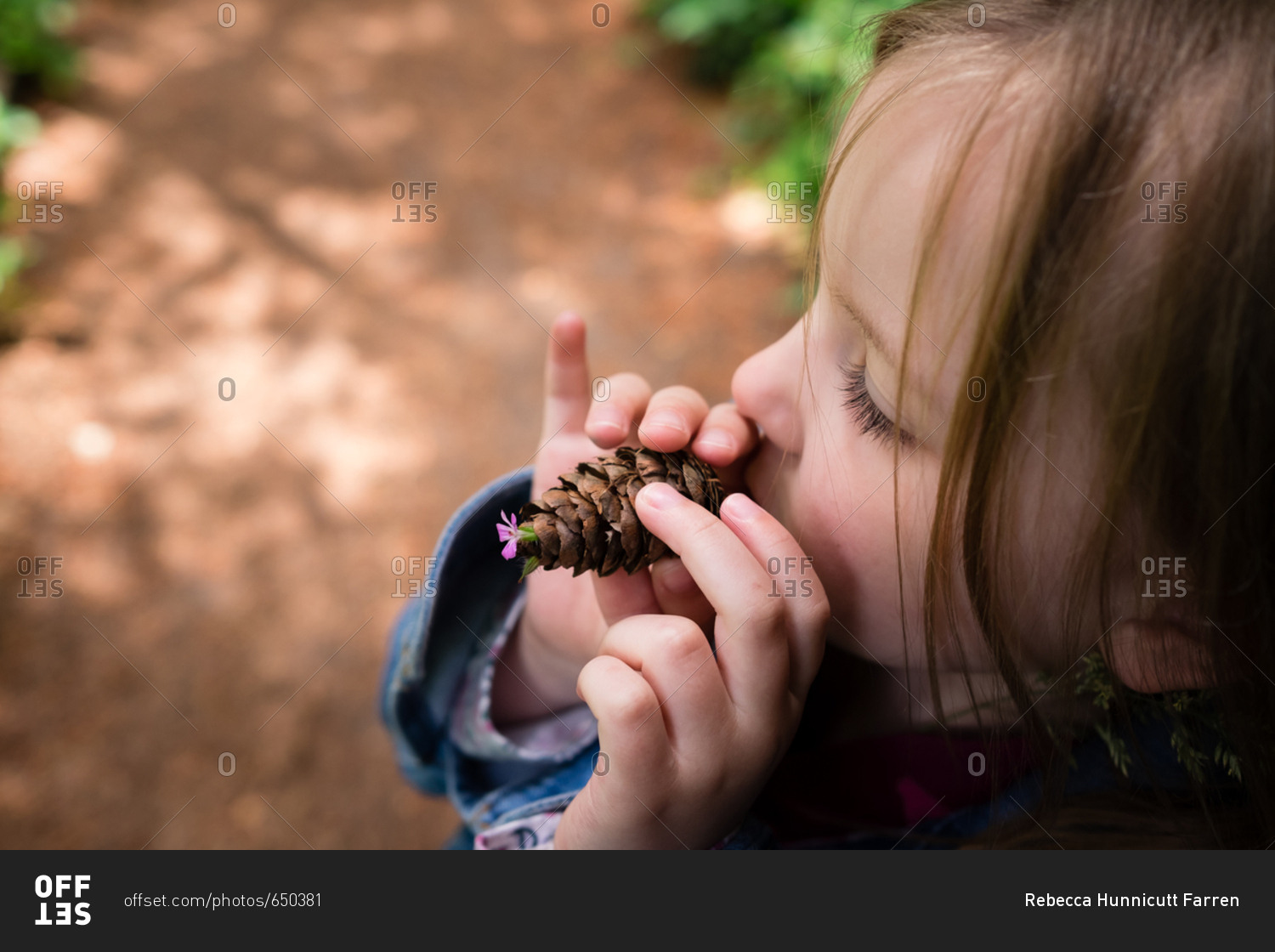 Little girl holding a pine cone with a small flower on the end
