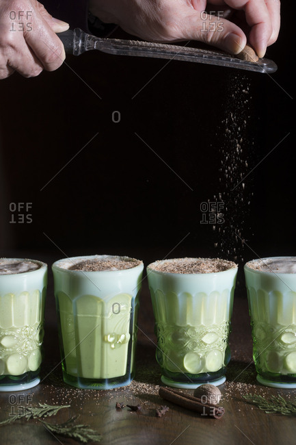 Side view of 4 glasses of eggnog with nutmeg being ground on top
