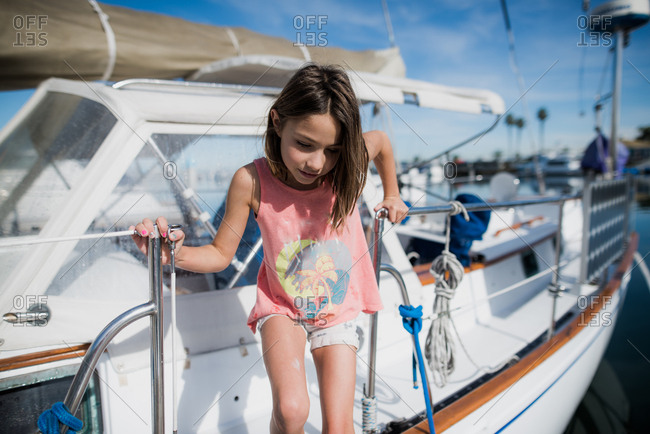 Girl stepping off of a sailboat at the marina in summertime in California
