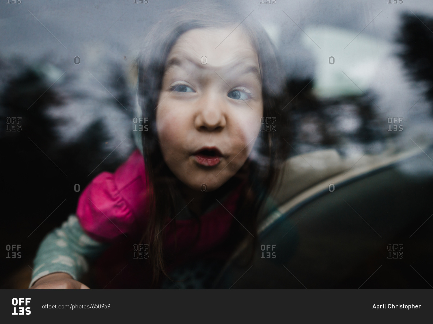 Little girl making silly faces against car window stock photo OFFSET