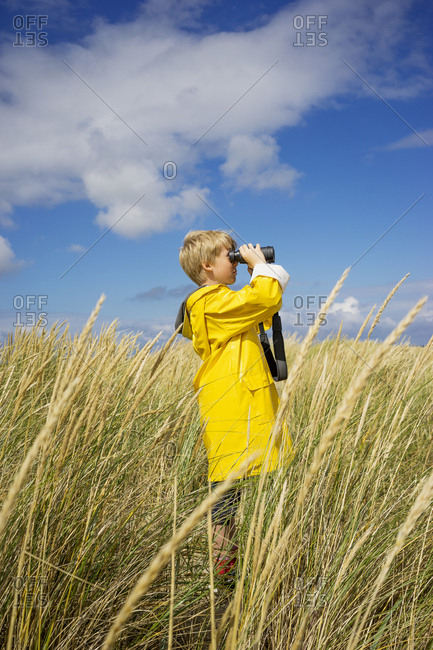 A young boy in wet weather gear looking through binoculars