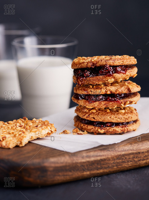 Half eaten cookie next to stack of cookies with jam and glasses of milk