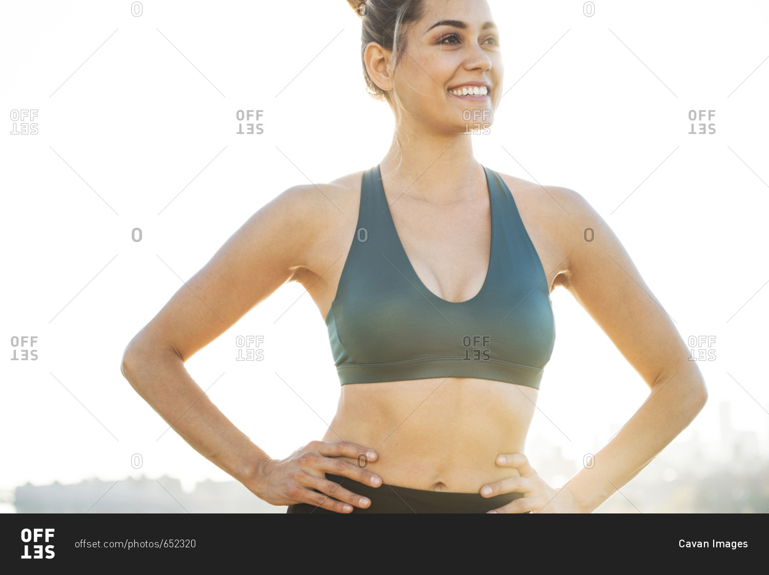 Cheerful young woman with hands on hip wearing sports bra against clear sky  stock photo