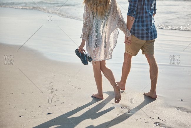 Young couple holding hands walking on empty beach loving hand in hand close relationship