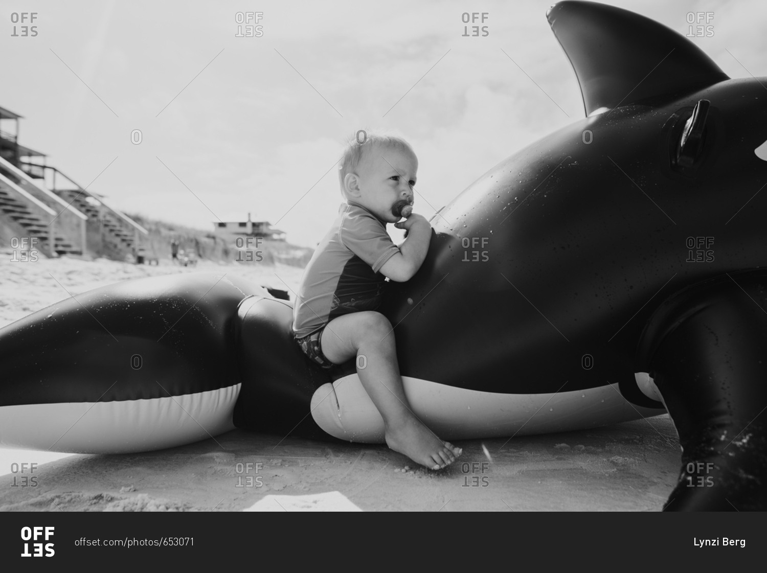 Baby boy sitting in an inflatable whale on a beach in black and white