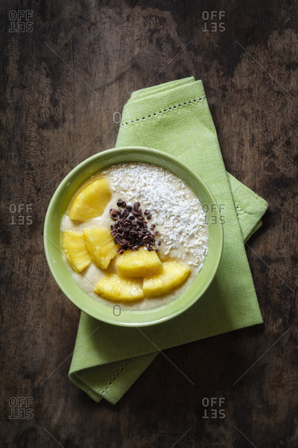 Bowl of fruit smoothie garnished with pineapple slices- coconut flakes and chocolate shaving