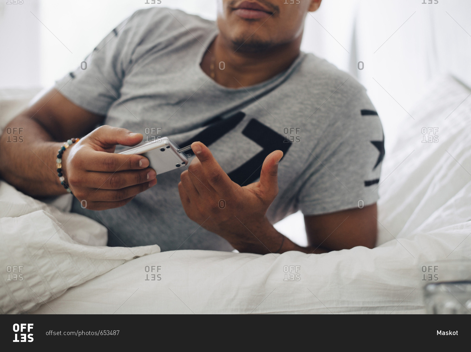 Midsection of man checking blood sugar level on glaucometer while lying on bed at home
