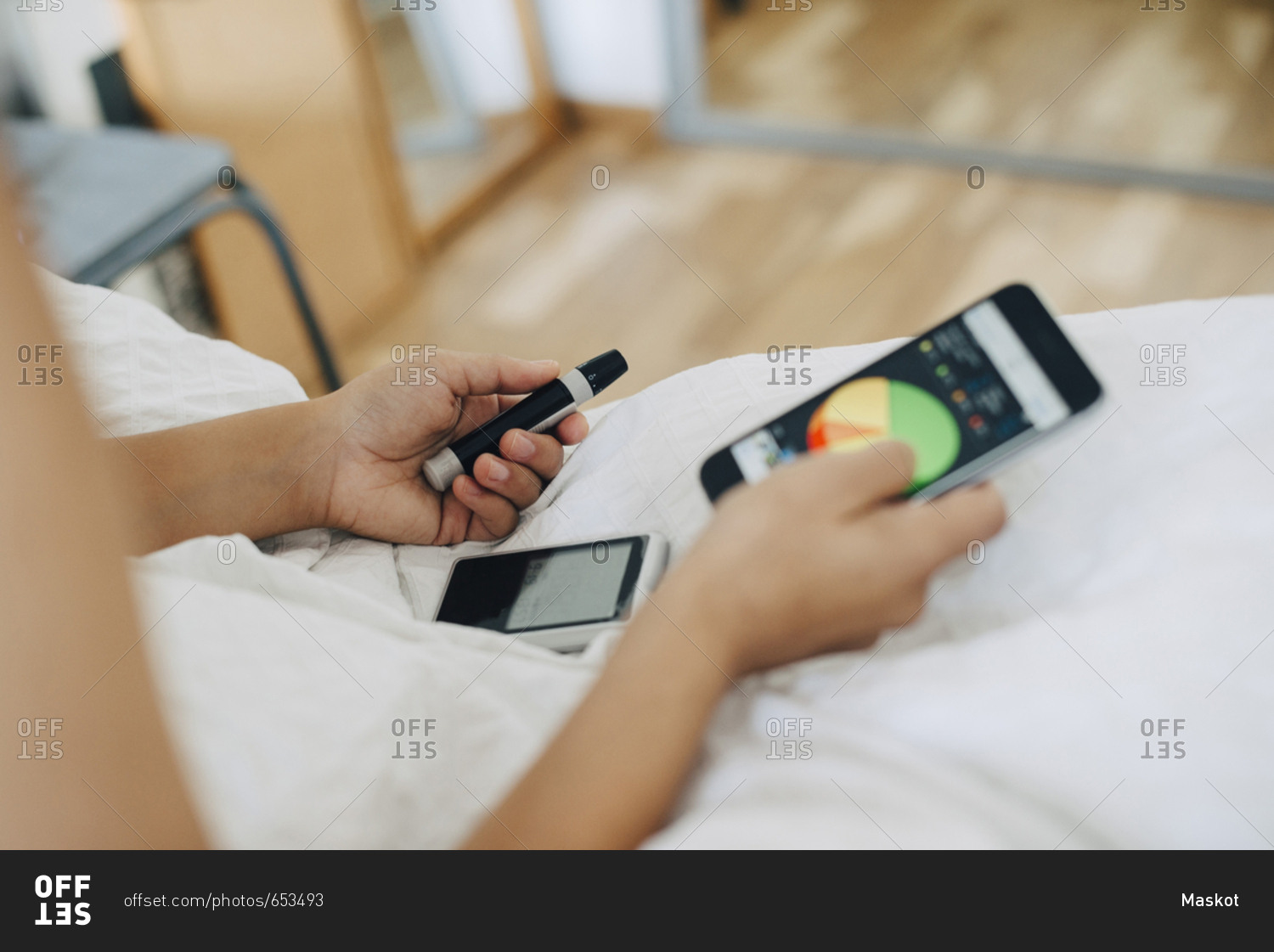Cropped woman checking blood sugar level while using mobile phone on bed