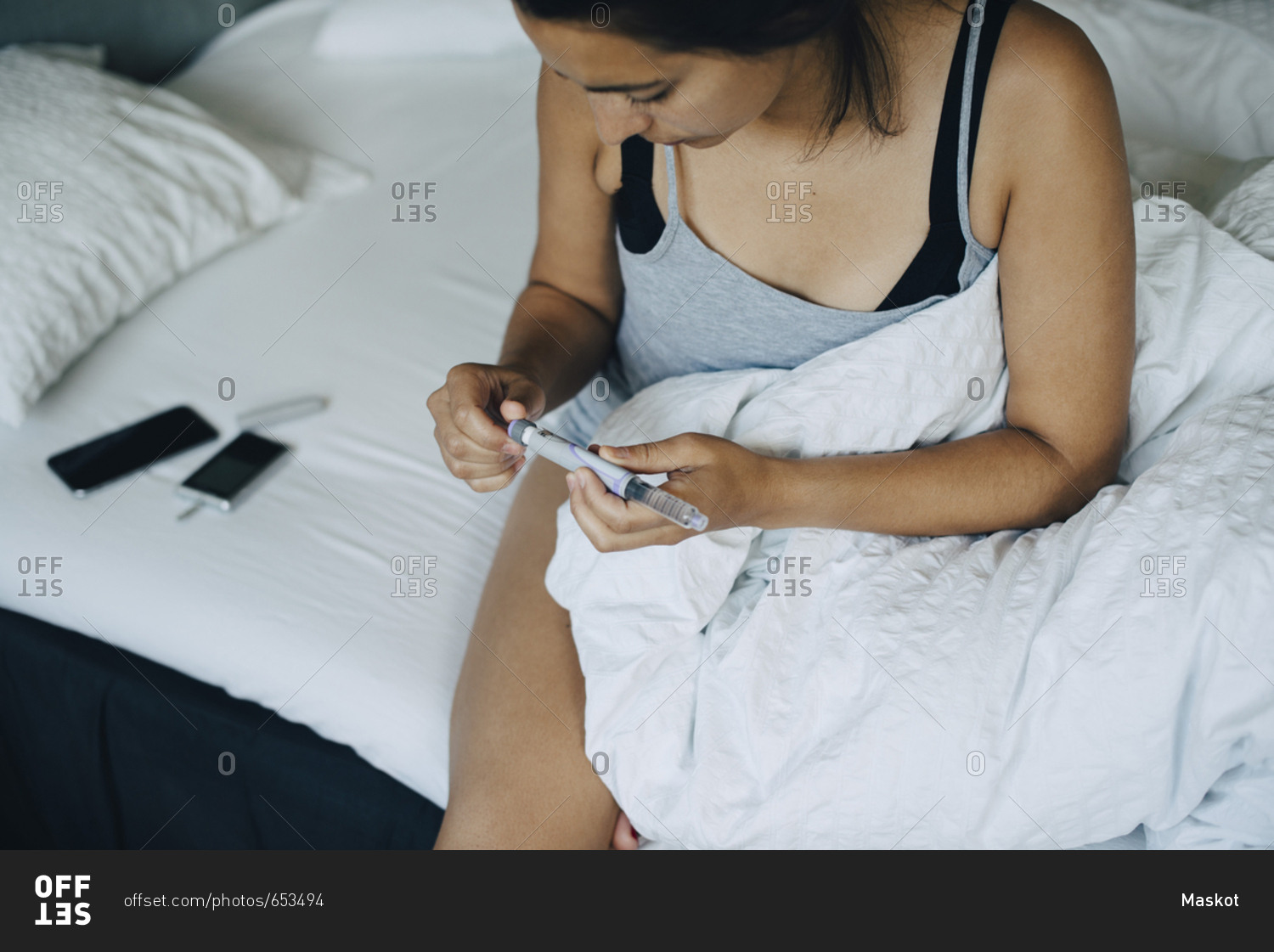 Woman looking at injection pen while sitting on bed in bedroom