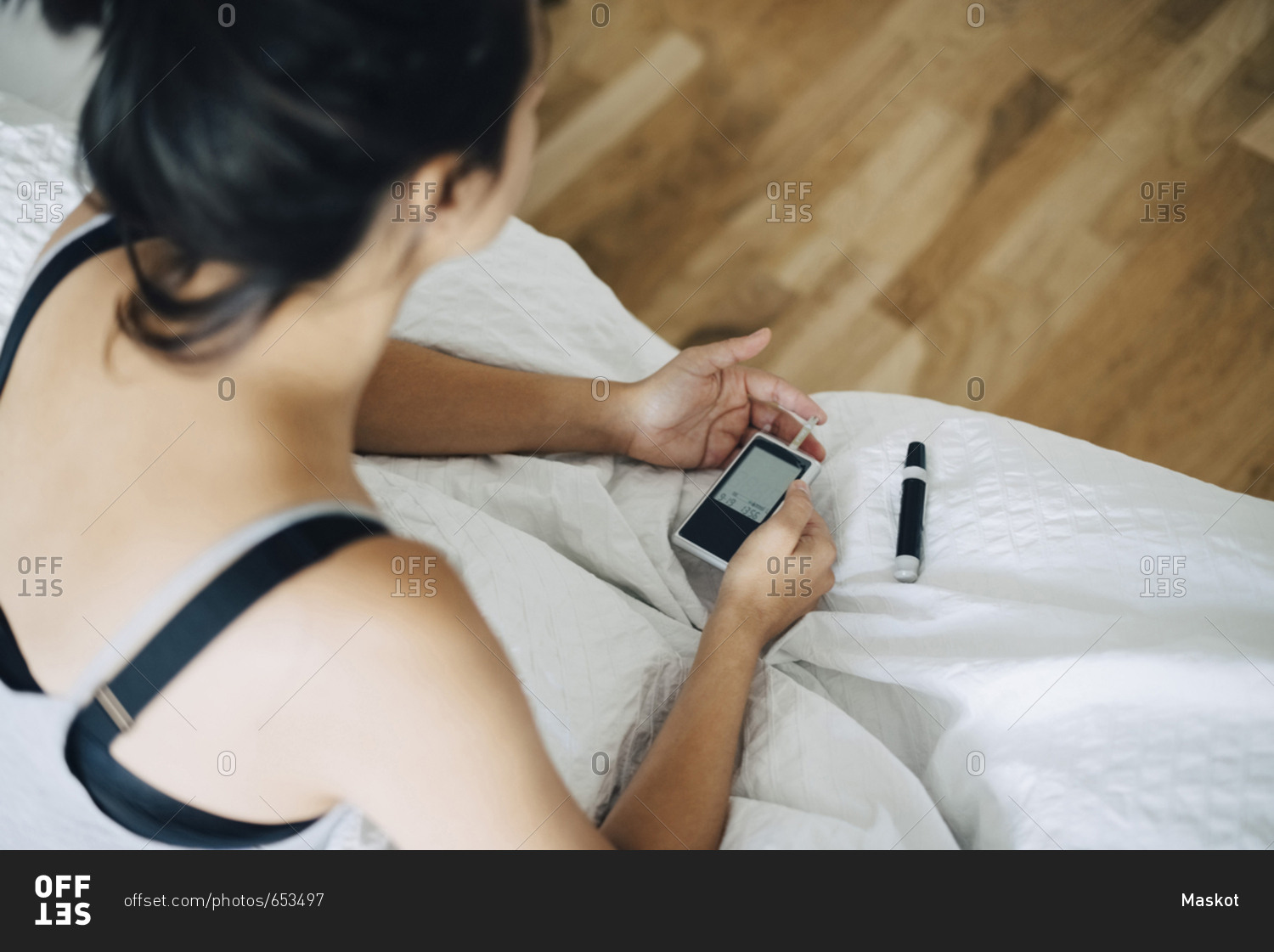 High angle view of woman checking blood sugar level while sitting on bed