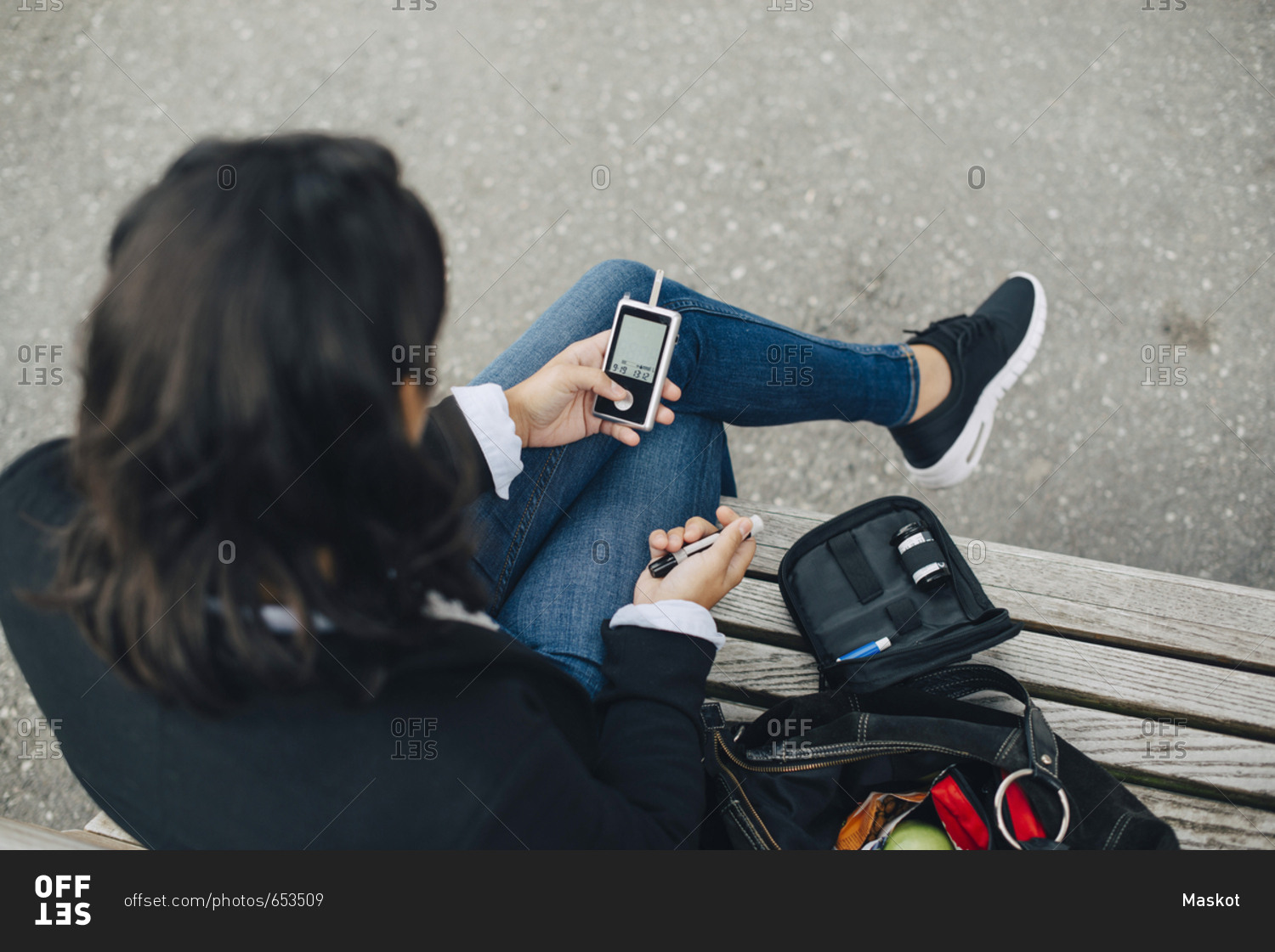 Woman checking blood sugar level while sitting on bench